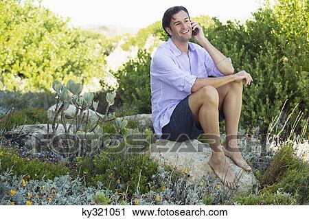 Mid adult man sitting on a rock and talking on a mobile phone View Large Photo Image Stock Image - Mid adult man sitting on a rock and talking on a mobile phone. Fotosearch