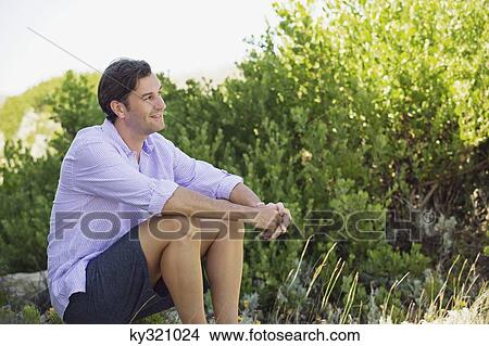Mid adult man sitting on a rock in a garden View Large Photo Image Picture - Mid adult man sitting on a rock in a garden. Fotosearch