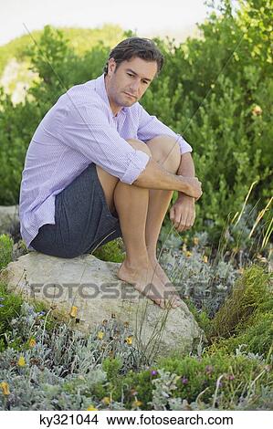Mid adult man sitting on a rock in a garden and thinking View Large Photo Image Picture - Mid adult man sitting on a rock in a garden and thinking. Fotosearch