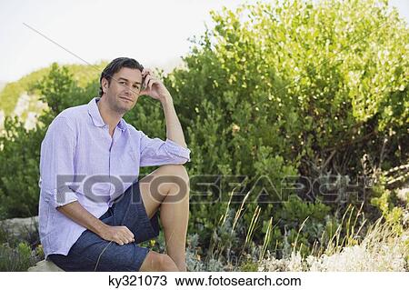 Mid adult man sitting on a rock in a garden and thinking View Large Photo Image Stock Image - Mid adult man sitting on a rock in a garden and thinking. Fotosearch