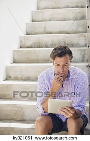 Mid adult man sitting on steps and using a digital tablet View Large Photo Image Stock Image - Mid adult man sitting on steps and using a digital tablet. Fotosearch