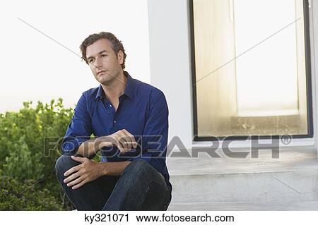 Stock Image - Mid adult man sitting outside the house and thinking. Fotosearch