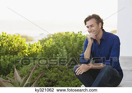 Mid adult man sitting with his hand on his chin and smiling View Large Photo Image Stock Image - Mid adult man sitting with his hand on his chin and smiling. Fotosearch