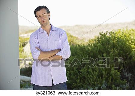 Stock Image - Portrait of a man standing with his arms crossed and thinking. Fotosearch