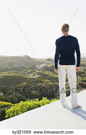 Rear view of a young man looking at view from the terrace of a house View Large Photo Image Stock Photo - Rear view of a young man looking at view from the terrace of a house. Fotosearch