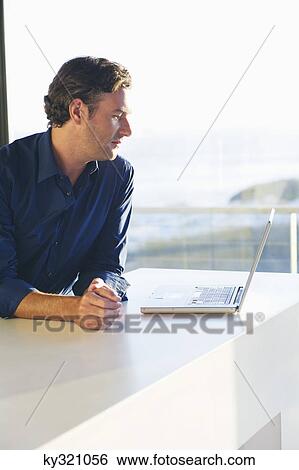 Side profile of a mid adult man looking at a laptop View Large Photo Image Stock Photograph - Side profile of a mid adult man looking at a laptop. Fotosearch