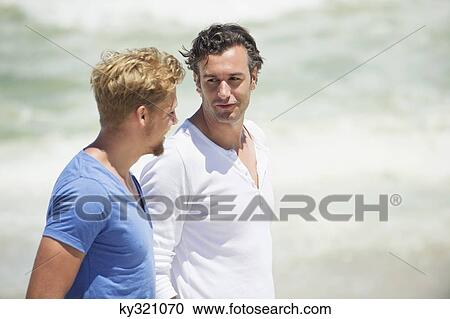 Two men talking while walking on the beach View Large Photo Image Stock Image - Two men talking while walking on the beach. Fotosearch