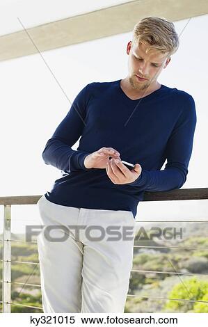 Young man using a mobile phone at a balcony View Large Photo Image Stock Photography - Young man using a mobile phone at a balcony. Fotosearch