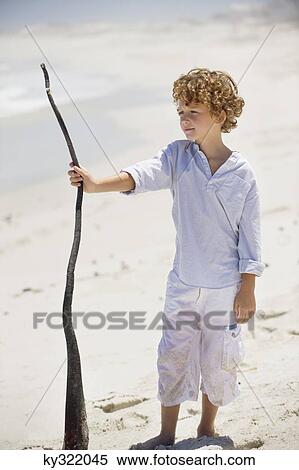 Boy holding a wooden stick on the beach View Large Photo Image Stock Photography - Boy holding a wooden stick on the beach. Fotosearch
