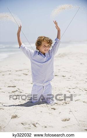 Stock Image - Boy playing in sand with his arms raised. Fotosearch