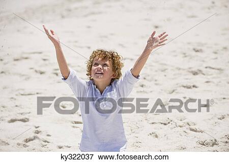 Boy standing with his arms raised on the beach View Large Photo Image Stock Photo - Boy standing with his arms raised on the beach. Fotosearch
