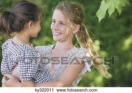 Stock Image - Cute girl carrying little sister and smiling. Fotosearch