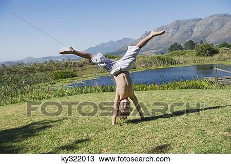 Stock Image - Cute little boy doing cartwheel against mountain. Fotosearch