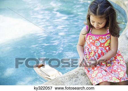 Girl sitting at edge of swimming pool looking at toy boat in water View Large Photo Image Stock Photo - Girl sitting at edge of swimming pool looking at toy boat in water. Fotosearch