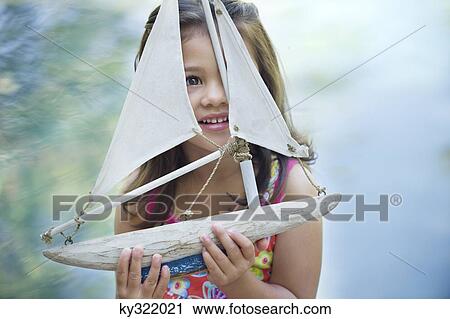 Stock Image - Little girl sitting by the swimming pool with model of boat in hand. Fotosearch