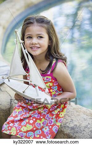 Stock Photo - Little girl sitting by the swimming pool with model of boat in hand. Fotosearch