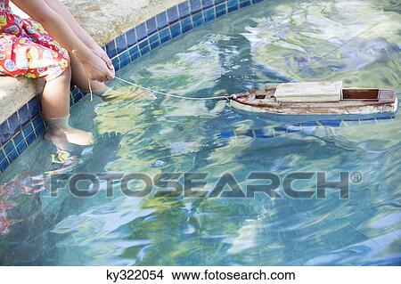 Low section view of a girl sitting at edge of swimming pool with toy boat in water View Large Photo Image Picture - Low section view of a girl sitting at edge of swimming pool with toy boat in water. Fotosearch