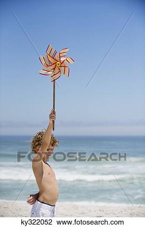 Stock Image - Side profile of a boy holding a pinwheel on the beach. Fotosearch