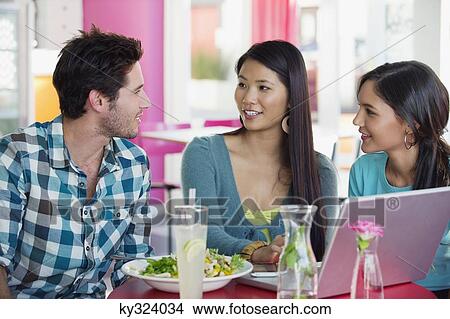 Friends looking at each other while eating food in a restaurant View Large Photo Image Picture - Friends looking at each other while eating food in a restaurant. Fotosearch