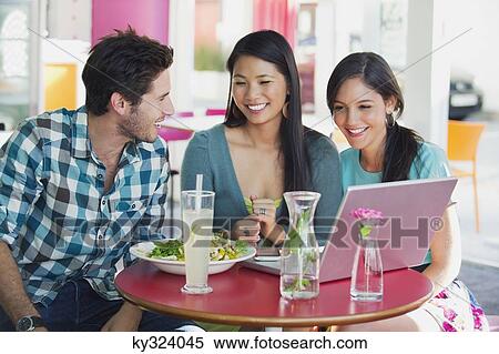 Friends using a laptop while eating food in a restaurant View Large Photo Image Stock Photography - Friends using a laptop while eating food in a restaurant. Fotosearch