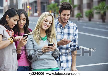 Friends using mobile phones outdoors View Large Photo Image Stock Photograph - Friends using mobile phones outdoors. Fotosearch