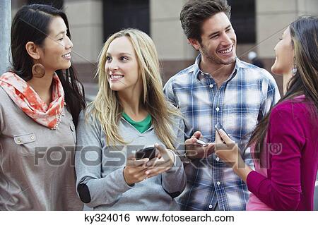 Friends using mobile phones outdoors View Large Photo Image Stock Photograph - Friends using mobile phones outdoors. Fotosearch