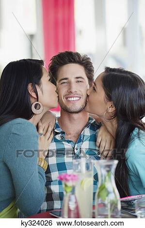 Man being kissed by two women in a restaurant View Large Photo Image Stock Photograph - Man being kissed by two women in a restaurant. Fotosearch