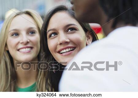Picture - Two women looking at a man and smiling. Fotosearch