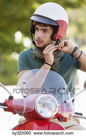 Man adjusting his helmet on a scooter View Large Photo Image Stock Image - Man adjusting his helmet on a scooter. Fotosearch
