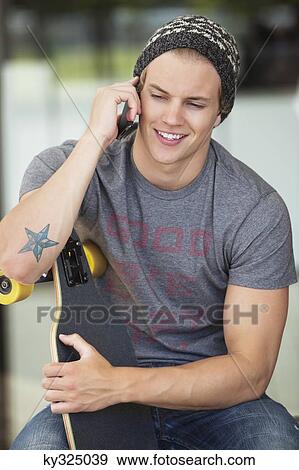 Man holding a skateboard and talking on a mobile phone View Large Photo Image Stock Photo - Man holding a skateboard and talking on a mobile phone. Fotosearch