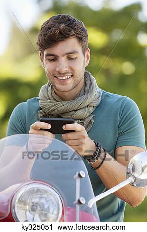 Stock Image - Man sitting on a scooter and text messaging. Fotosearch