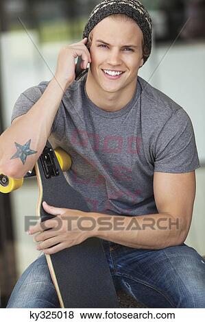 Portrait of a man holding a skateboard and talking on a mobile phone View Large Photo Image Stock Photo - Portrait of a man holding a skateboard and talking on a mobile phone. Fotosearch