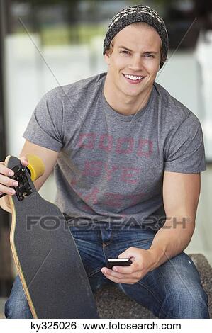 Portrait of a man holding skateboard and using mobile phone View Large Photo Image Stock Photograph - Portrait of a man holding skateboard and using mobile phone. Fotosearch