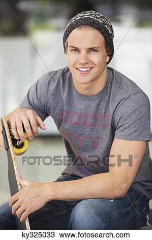 Portrait of a smiling man holding skateboard View Large Photo Image Stock Image - Portrait of a smiling man holding skateboard. Fotosearch