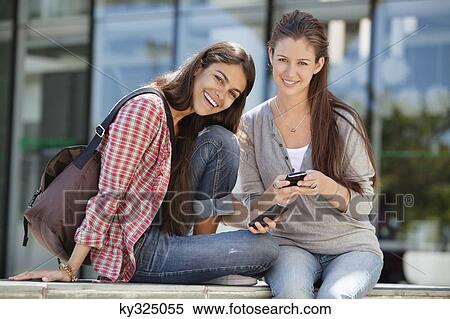 Portrait of two women holding mobile phone and smiling View Large Photo Image Stock Photography - Portrait of two women holding mobile phone and smiling. Fotosearch