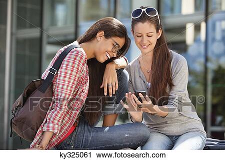 Two female friends reading text message on a mobile phone View Large Photo Image Stock Image - Two female friends reading text message on a mobile phone. Fotosearch