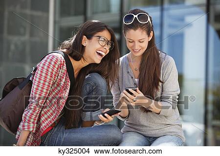 Two female friends using mobile phones View Large Photo Image Picture - Two female friends using mobile phones. Fotosearch