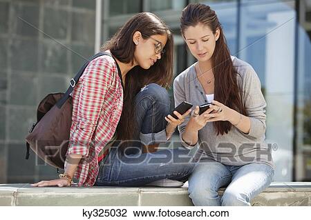 Two young female friends reading messages View Large Photo Image Stock Image - Two young female friends reading messages. Fotosearch