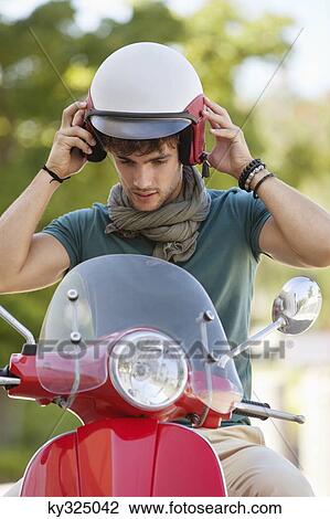 Stock Image - Young man wearing helmet sitting on scooter. Fotosearch