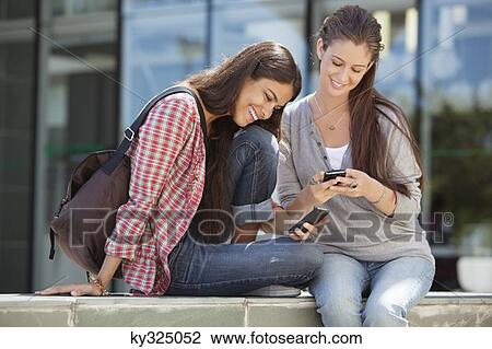 Young women using their mobile phones and smiling View Large Photo Image Stock Image - Young women using their mobile phones and smiling. Fotosearch