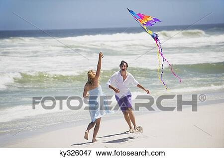 Stock Photo - Couple flying kite on the beach. Fotosearch
