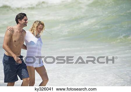 Couple walking on the beach with their arms around each other View Large Photo Image Stock Image - Couple walking on the beach with their arms around each other. Fotosearch