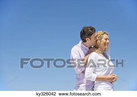 Stock Image - Man kissing a woman from behind and smiling. Fotosearch