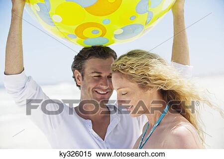Stock Photography - Man lifting a beach ball and smiling with a woman near him. Fotosearch