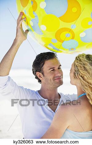 Man lifting a beach ball with a woman near him View Large Photo Image Stock Image - Man lifting a beach ball with a woman near him. Fotosearch