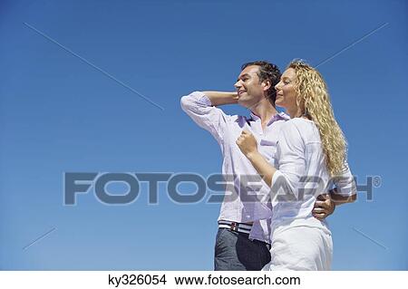 Man standing with his arm around a woman View Large Photo Image Picture - Man standing with his arm around a woman. Fotosearch