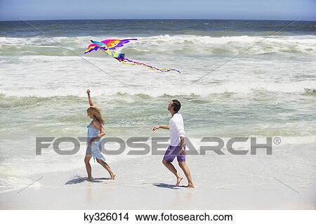 Mid adult couple flying kite on the beach View Large Photo Image Picture - Mid adult couple flying kite on the beach. Fotosearch