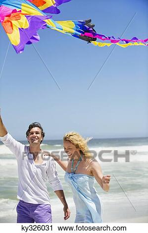 Stock Image - Mid adult couple flying kite on the beach. Fotosearch