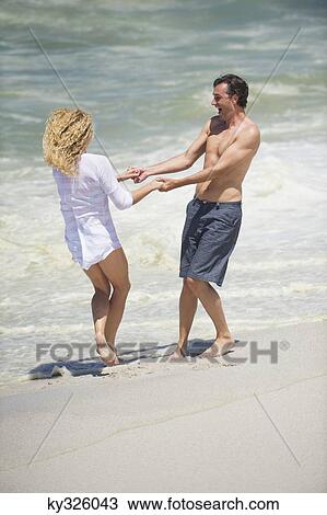 Stock Image - Mid adult couple playing on the beach. Fotosearch
