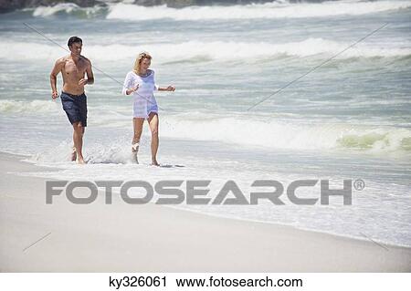 Mid adult couple running on the beach View Large Photo Image Stock Image - Mid adult couple running on the beach. Fotosearch